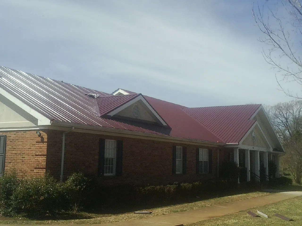 Red metal roof with gabled entries on a long brick building, from a Hail Damage Roof Repair job in Anacortes