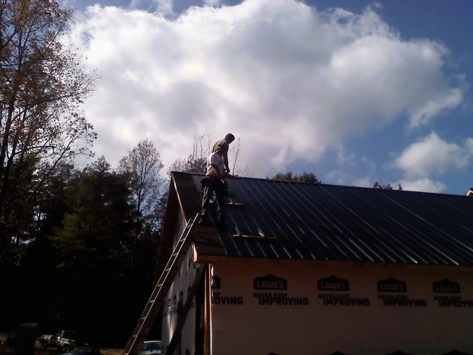 Roofer fastening dark metal panels high against a cloudy sky, from a Roof Inspection job in Anacortes